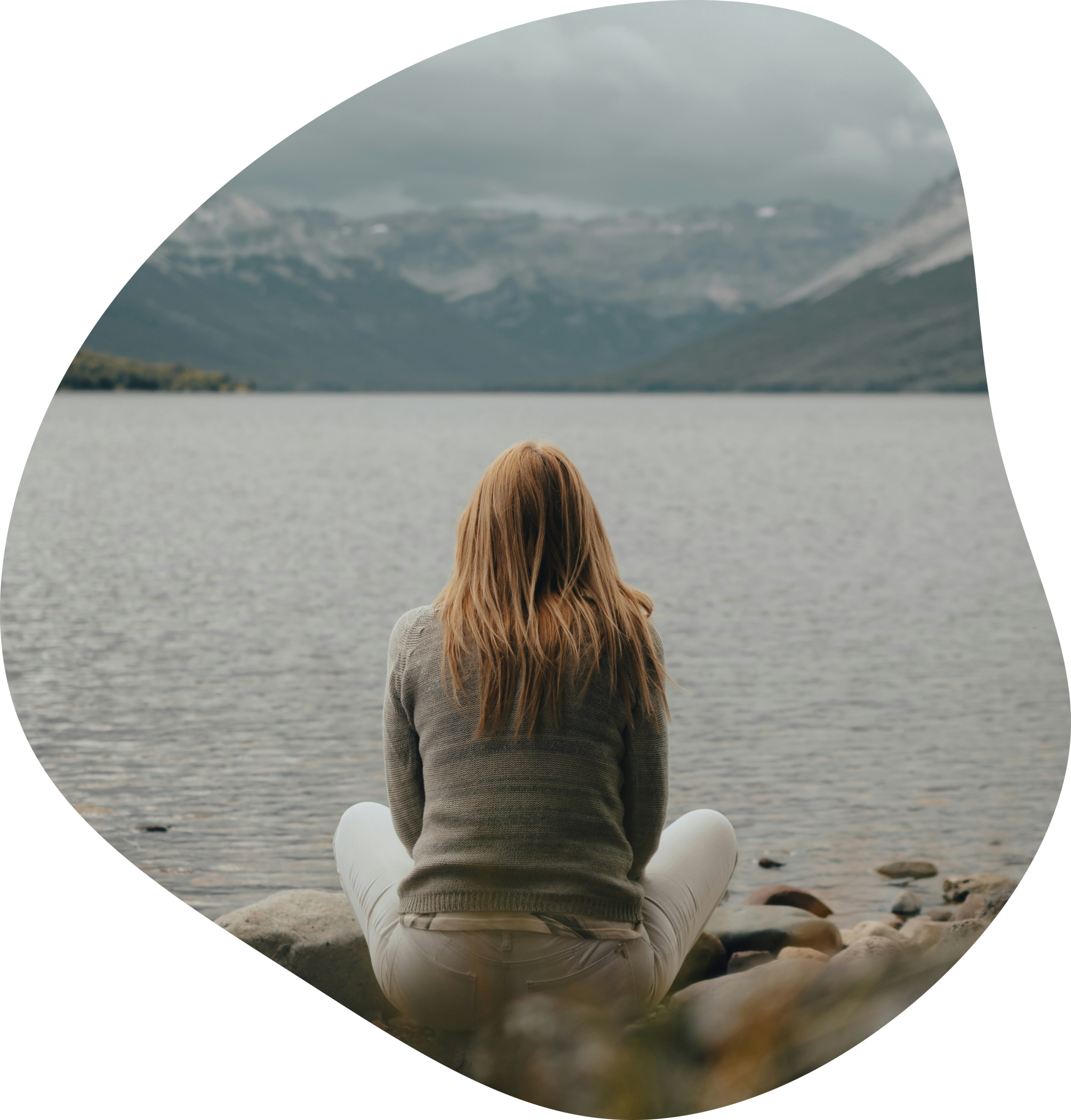 Une femme assise en tailleur face à un lac et des montagnes