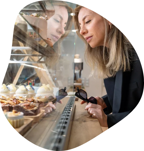 Une femme blonde vêtue de manière corporate se penche pour choisir parmi tous les desserts proposés par la cafeteria.