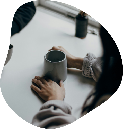 Close up sur une tasse hrise vu de haut avec des mains placés à chaque extrémités. Cette photo est dans le cadre de travail