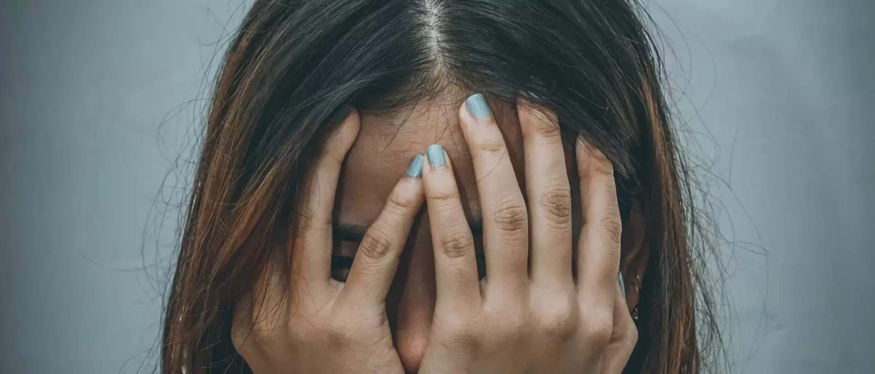 Un portrait d'une femme se tenant le visage dans ses deux mains. Elle semble être dehors, dans le froid et vraiment triste. on ne voit pas son visage mais on le devine
