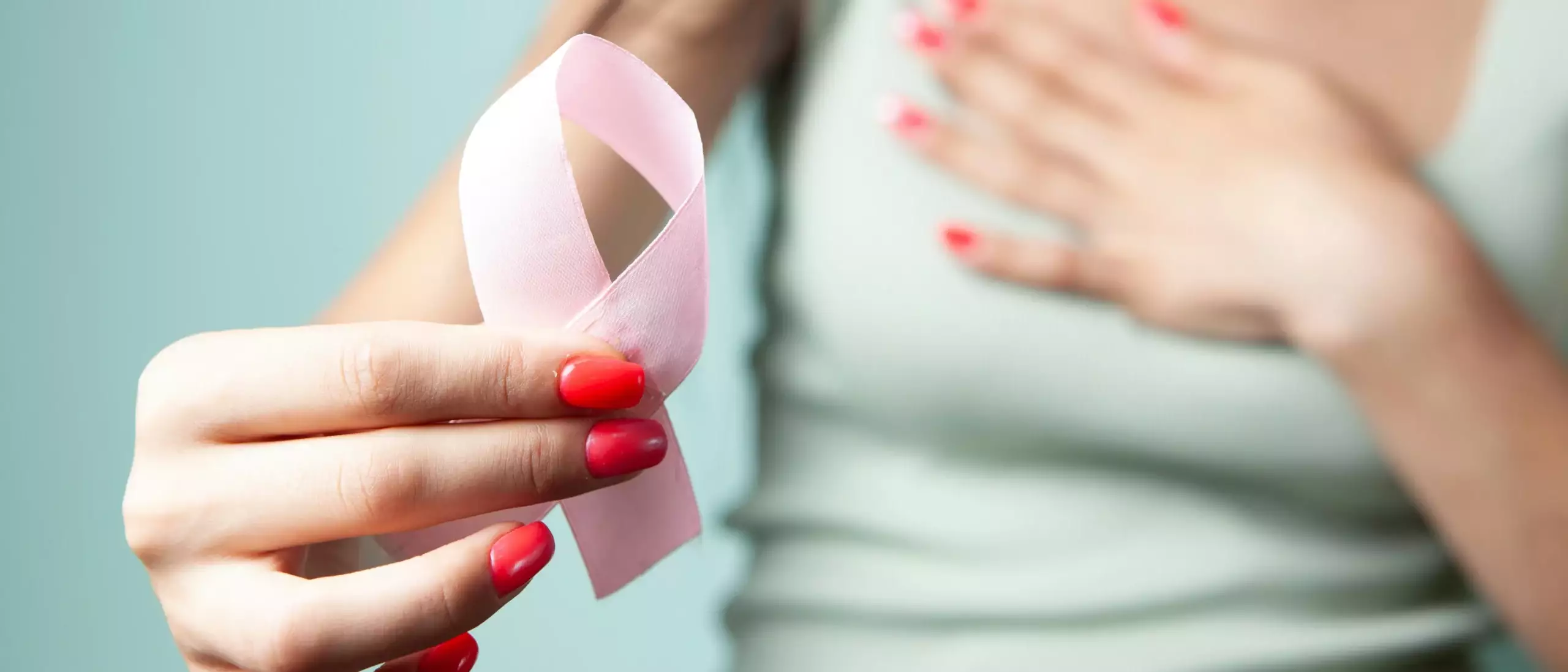 Une femme montre en premier plan un ruban rose en lui donnant la forme d'une boucle pour montrer son soutien à octobre rose